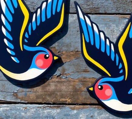 Two colorful handmade swallow wall art pieces on rustic blue wood, WallShapes UK decor