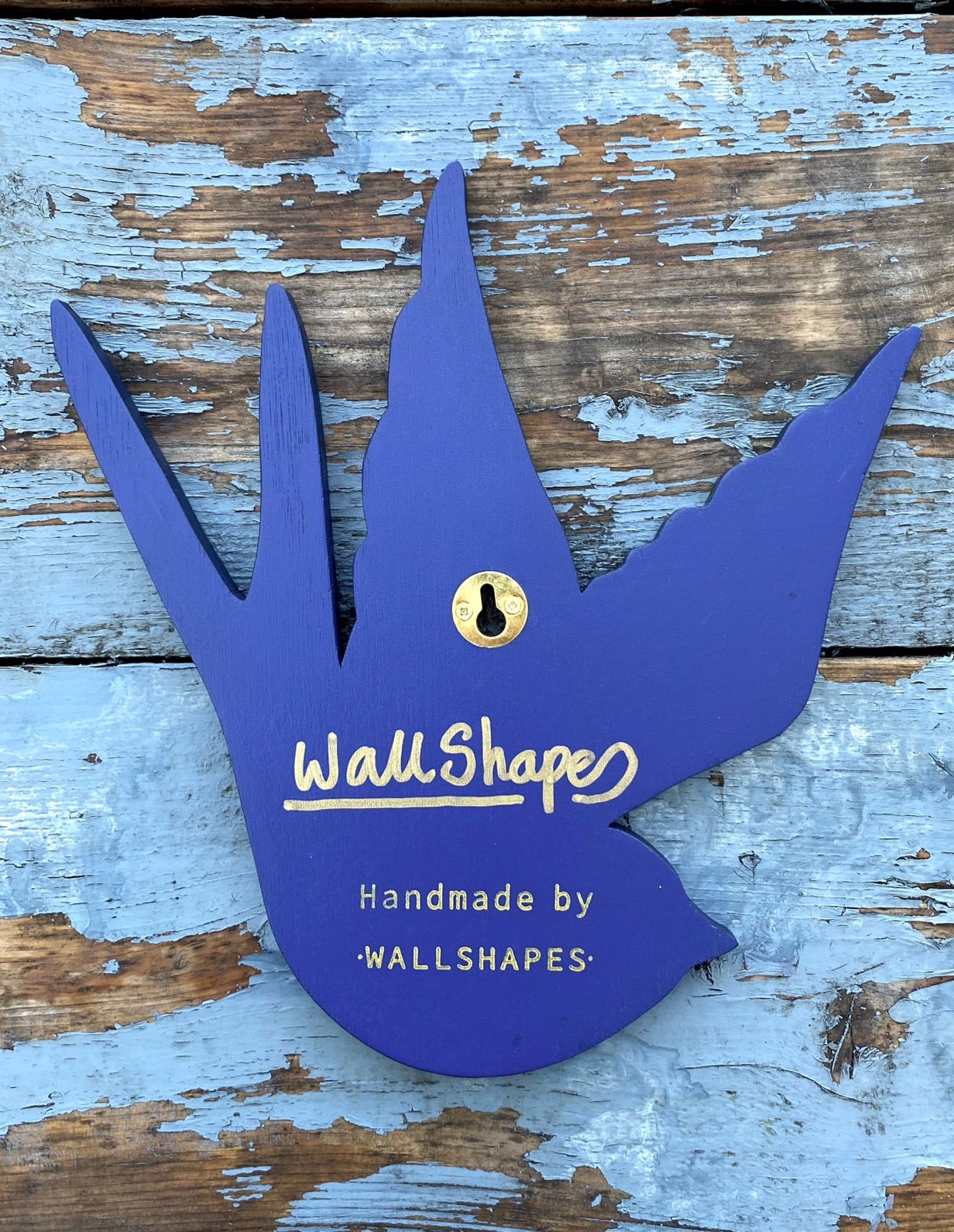 Back view of a tattoo inspired, colourful spray painting, painted on a hand-shaped wooden panel, showing hanging method and signature, displayed on a blue weathered wooden surface.