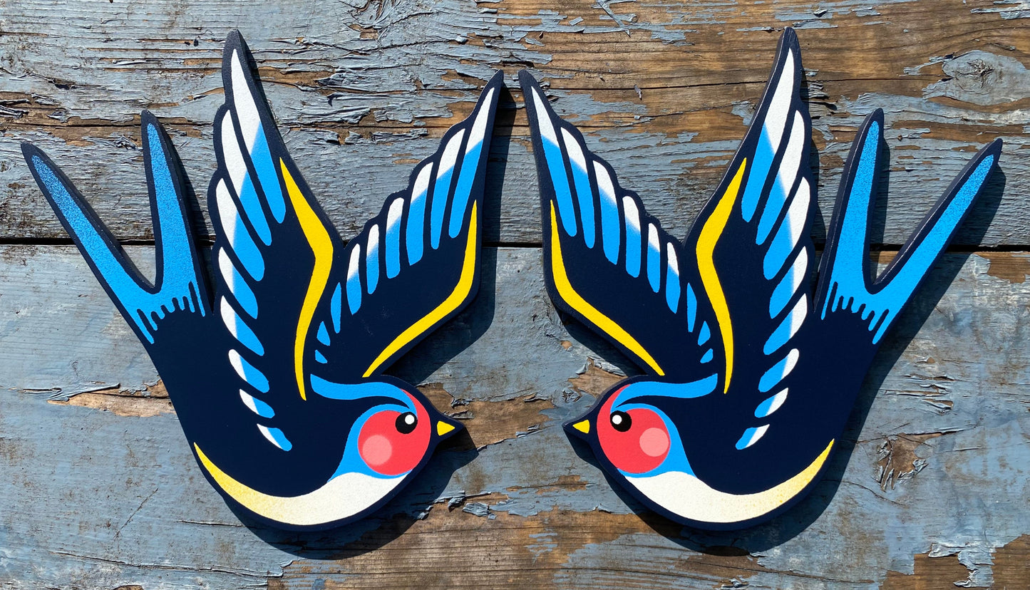 Hand-cut plywood swallow wall art painted in blue, yellow, and black with red cheek detail, inspired by vintage tattoo flash style.