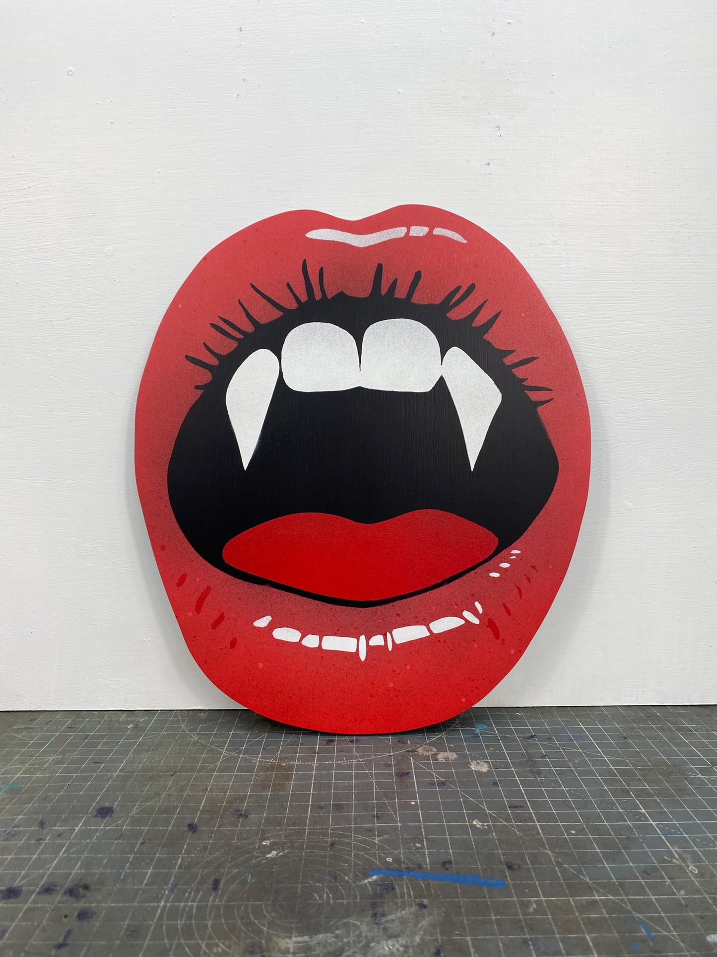 Spray-painting of red lips with vampire fangs with a stencil cutting board on a white background.