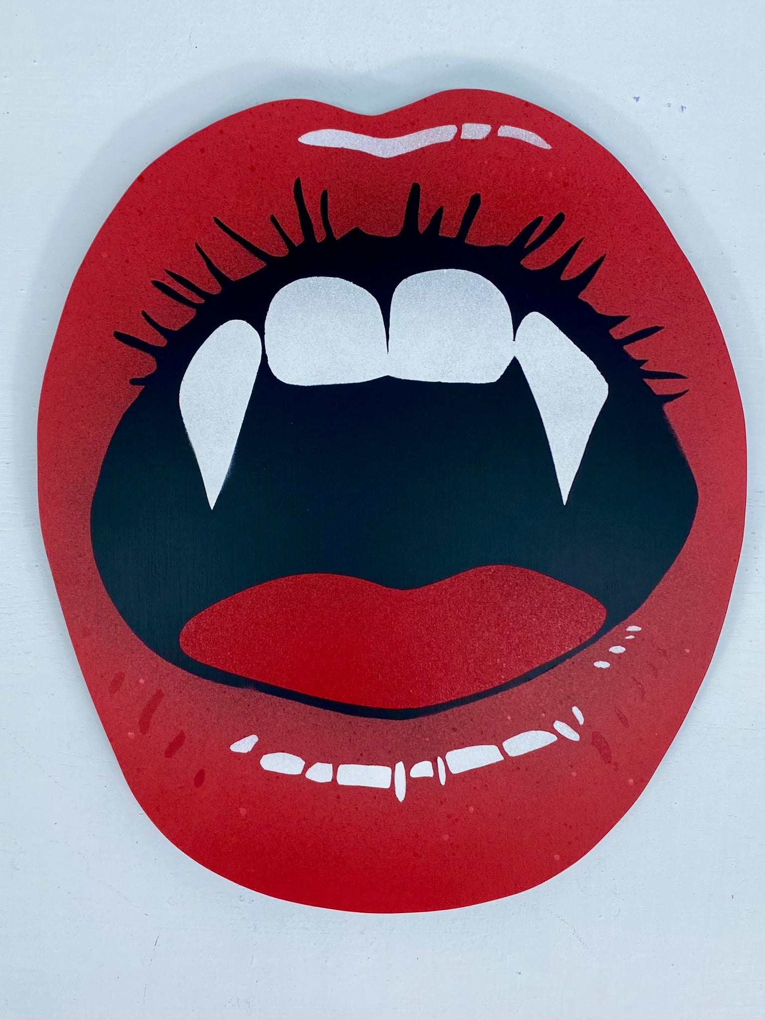 Spray-painting of red lips with vampire fangs on a white background.