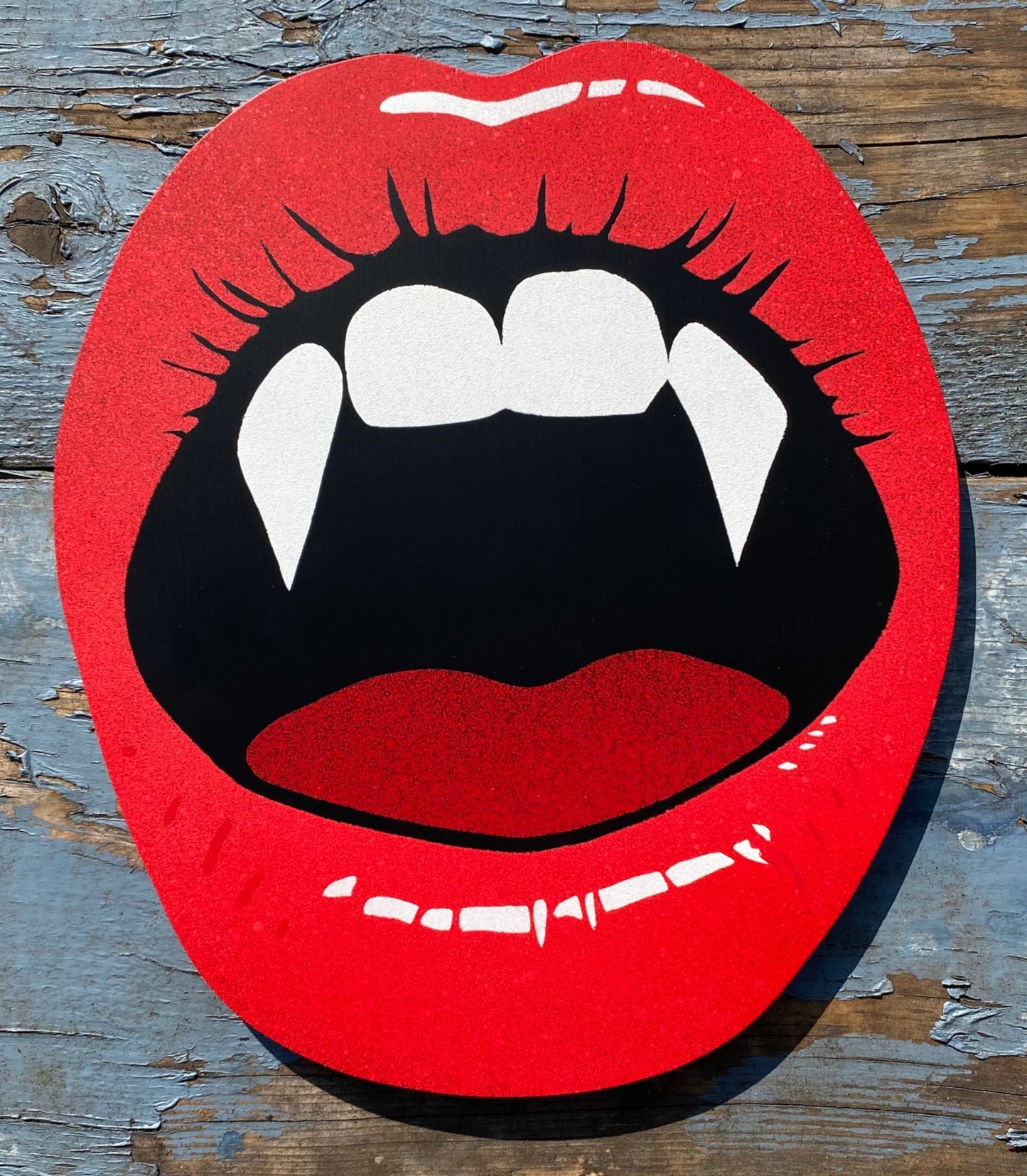Hand made shaped spray-painting of red lips with vampire fangs on a weathered painted background.