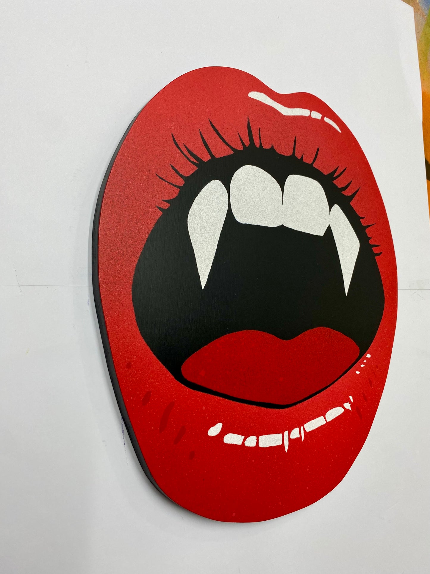 Hand made shaped spray-painting of red lips with vampire fangs on a white background.