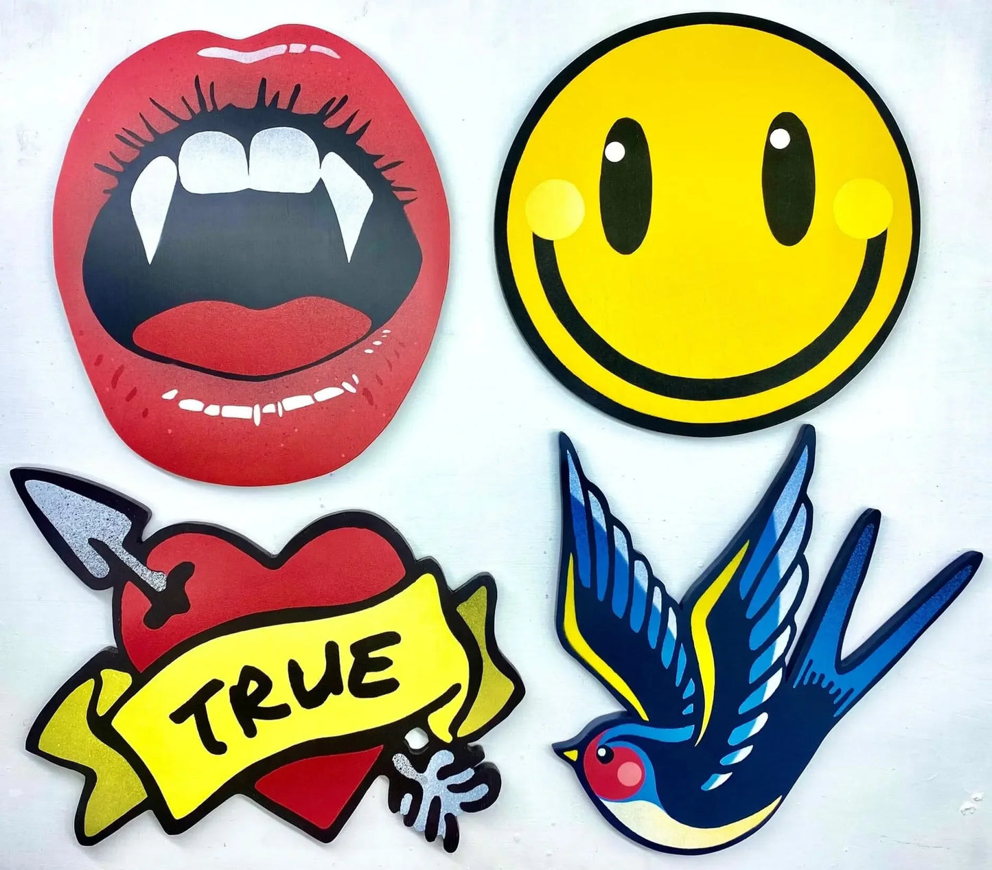 Colorful spray-painted wall art pieces featuring lips with fangs, smiley face, heart with 'TRUE' banner, and blue bird by WallShapes Shop.