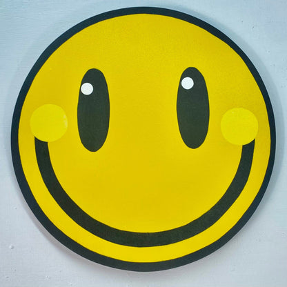 A square close up photo of a big yellow smiley spray-painting on a white painted wall.