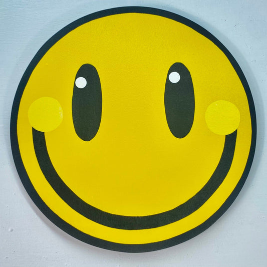 A square close up photo of a big yellow smiley spray-painting on a white painted wall.