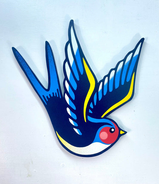 A close up of a spray-painted shaped wooden cut out swallow on a white wall.