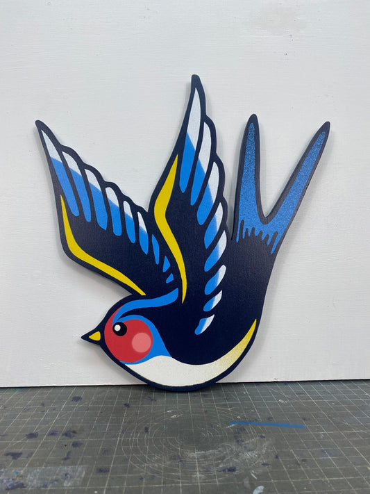 Tattoo inspired, colourful spray painting, painted on a hand-shaped wooden panel displayed on a stencil cutting mat, with a white wall.