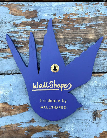 Back view of a tattoo inspired, colourful spray painting, painted on a hand-shaped wooden panel, showing hanging method and signature, displayed on a blue weathered wooden surface.
