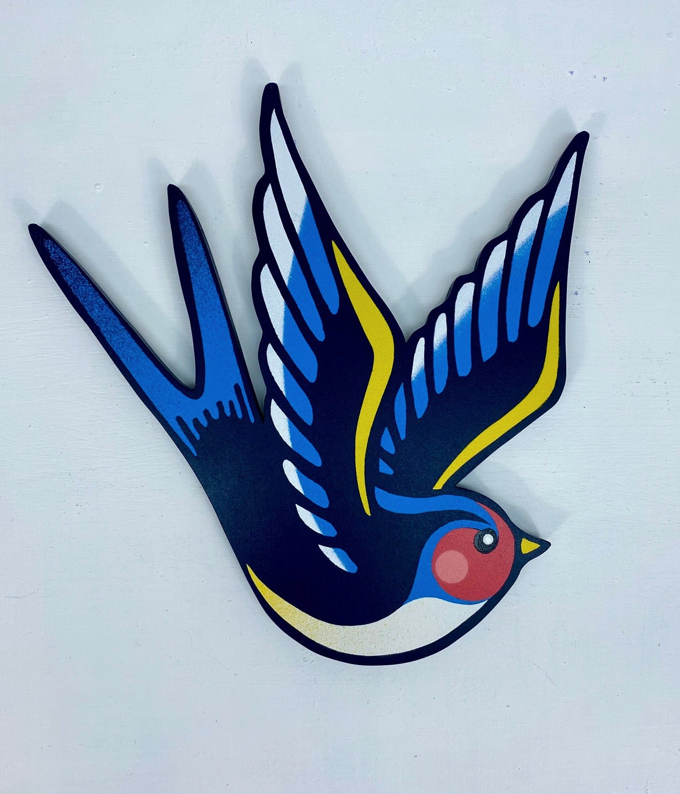 Tattoo inspired, colourful spray painting, painted on a hand-shaped wooden panel displayed on a white wall.