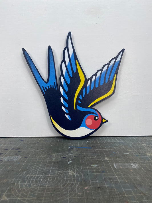 Tattoo inspired, colourful spray painting, painted on a hand-shaped wooden panel displayed on a stencil cutting mat, with a white wall.