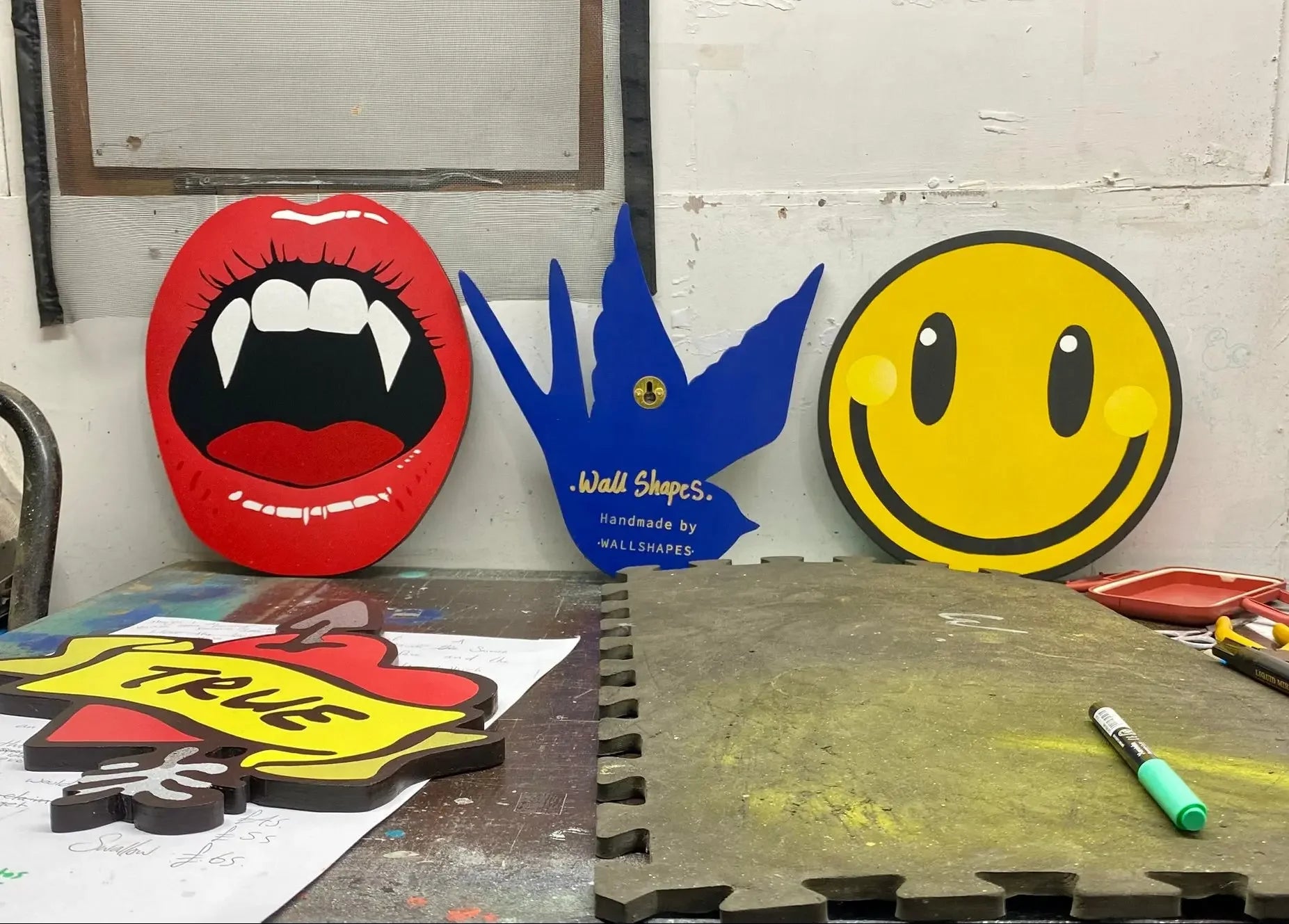Handcrafted wall art by WallShapes featuring pop art vampire lips, blue swallow, pierced heart and smiley face designs.
