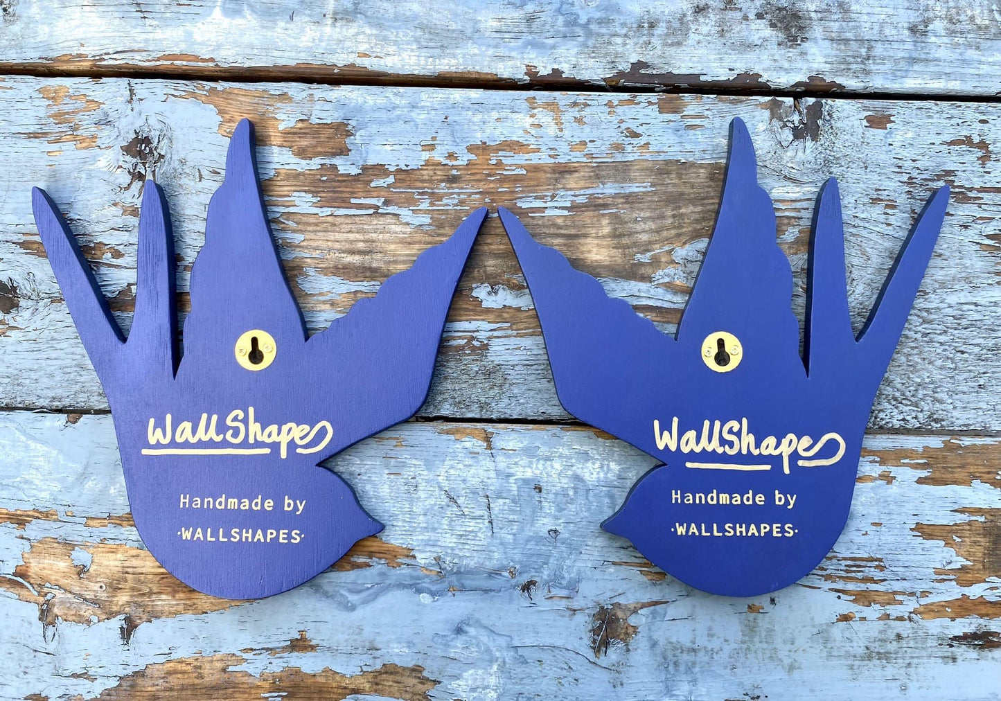 A pair of blue handmade WallShapes decorative swallow bird wall art pieces displayed on a rustic wooden  background.