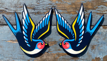 Hand-cut plywood swallow wall art painted in blue, yellow, and black with red cheek detail, inspired by vintage tattoo flash style.
