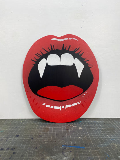 Spray-painting of red lips with vampire fangs with a stencil cutting board on a white background.