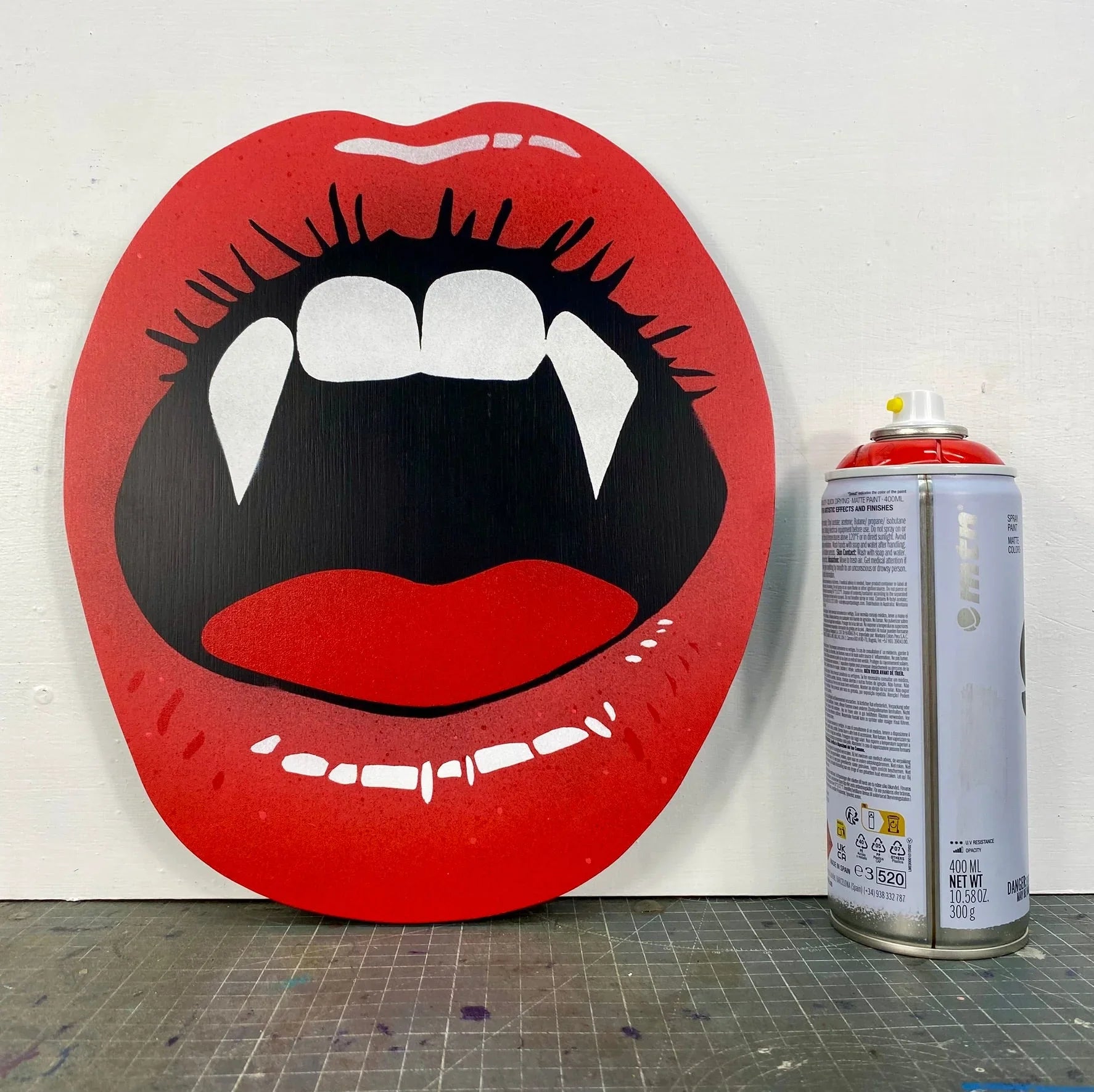 Handmade spray-painted wall art of red vampire lips by WallShapes, shown beside paint can for size comparison.