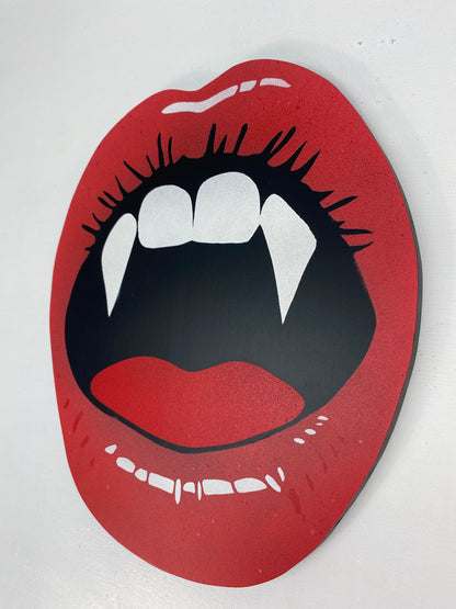 Hand made shaped spray-painting of red lips with vampire fangs on a white background.