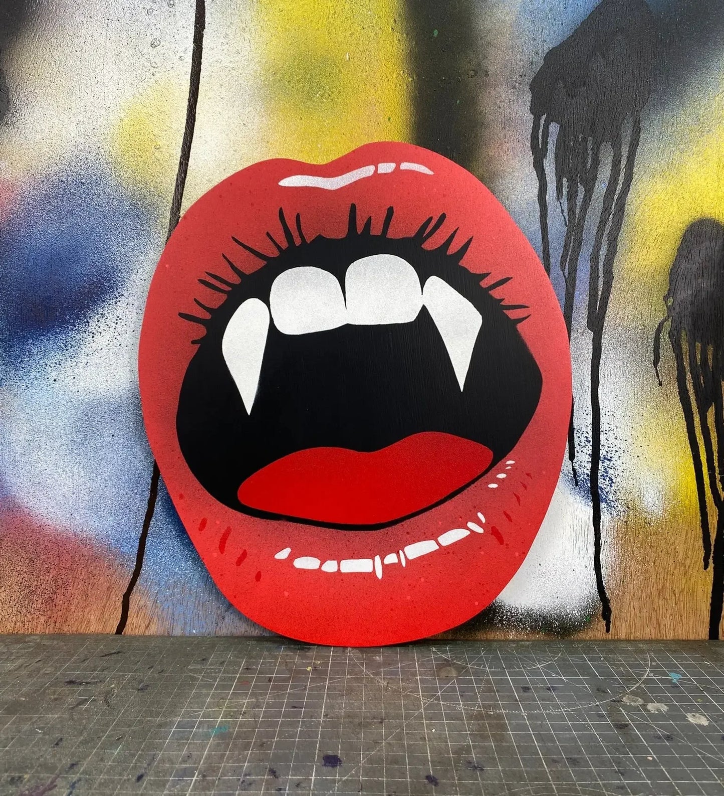 Vampire lips spray-painted wall art with red lips and fangs on colorful graffiti background