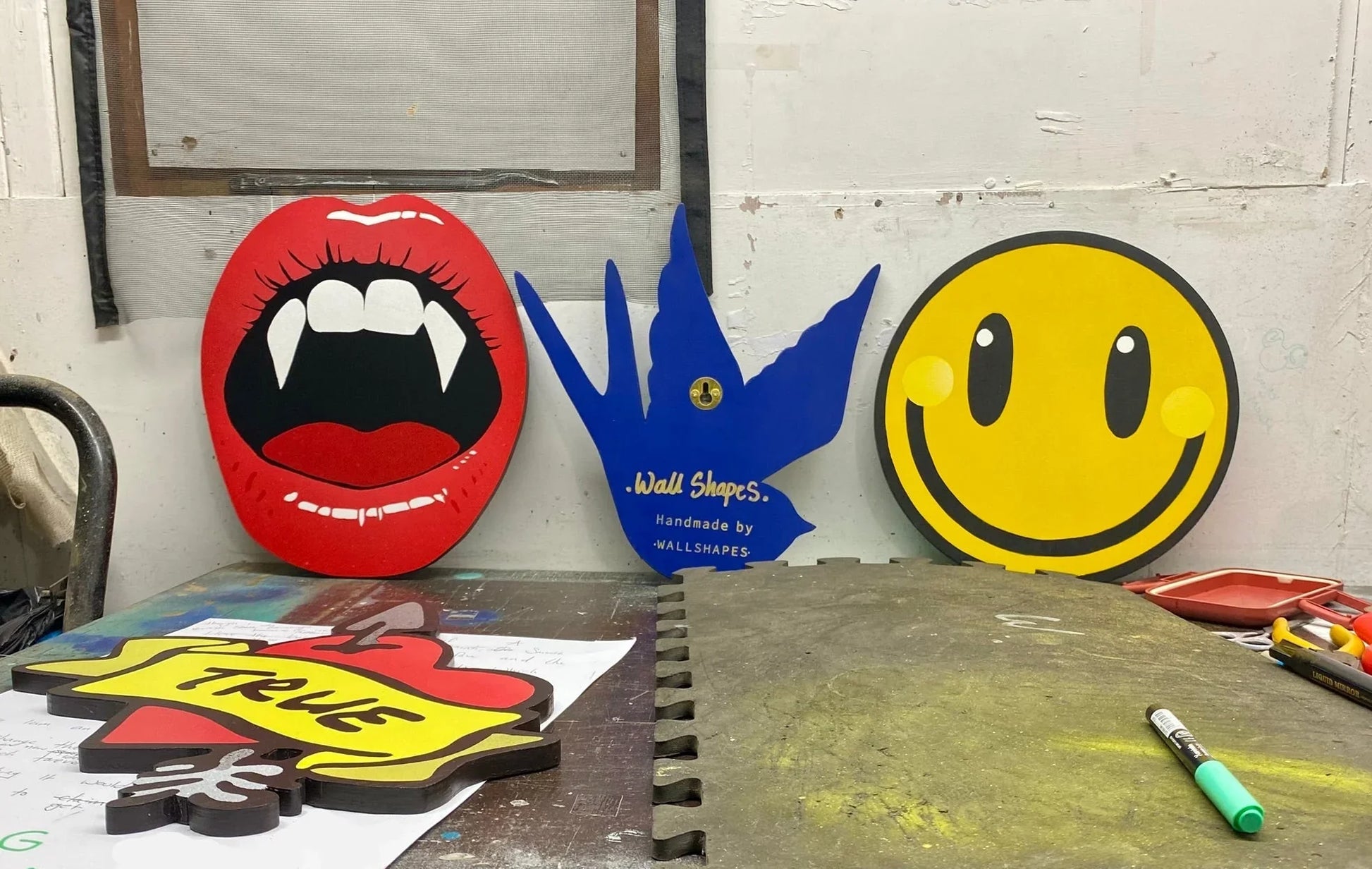 Handcrafted spray-painted wall art by WallShapes, featuring vampire lips, blue bird, smiley face, and 'True' heart designs.