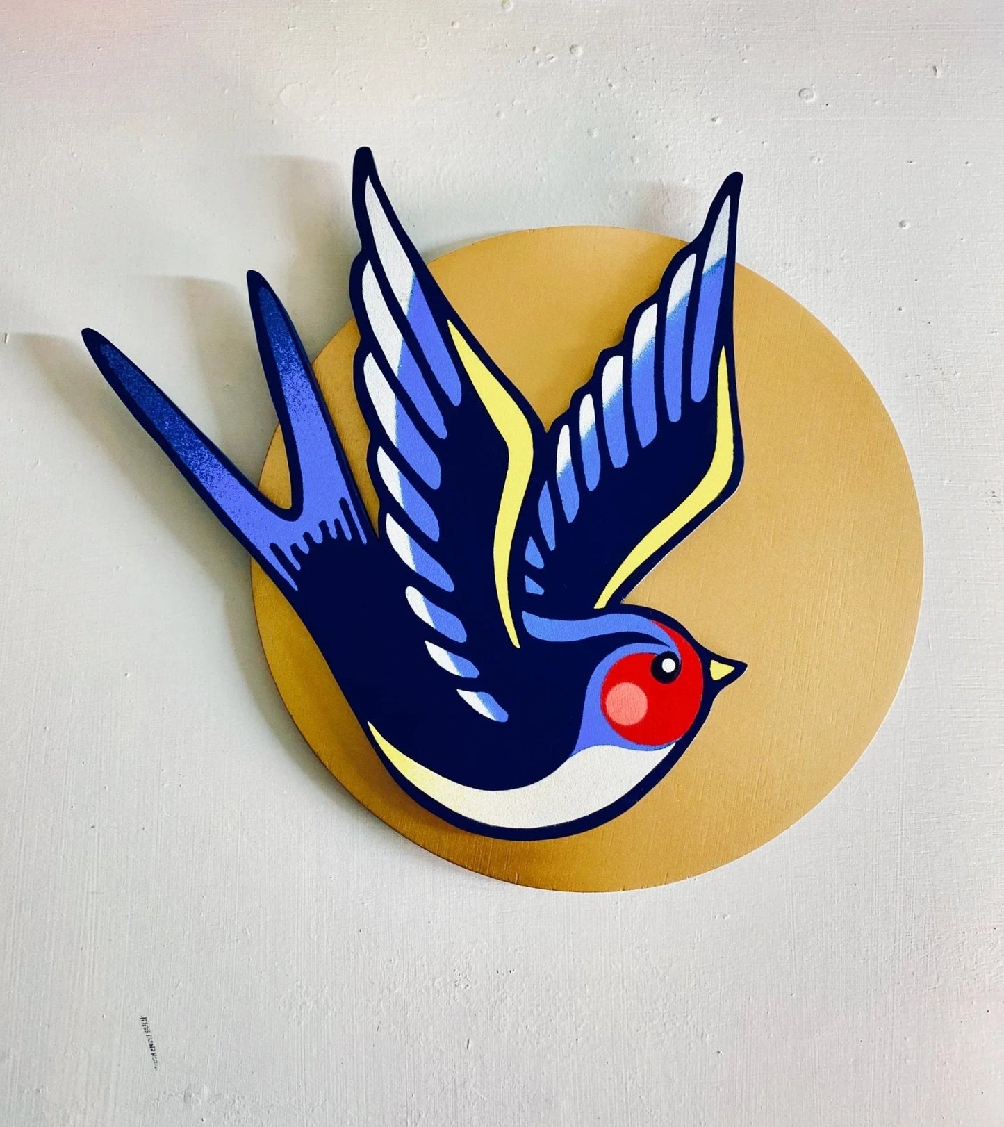 Handmade spray-painted wall art of a colorful swallow bird on a metallic gold circle background.