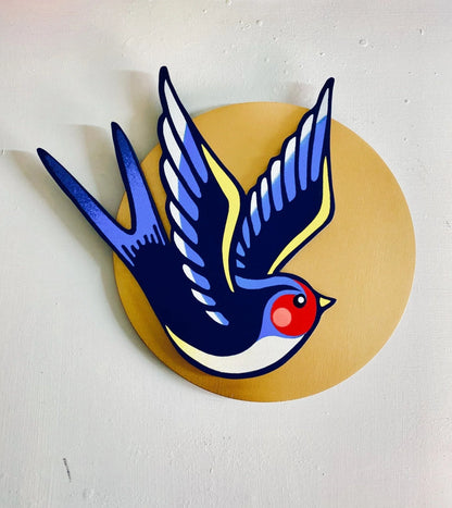 Handmade spray-painted wall art of a colorful swallow bird on a metallic gold circle background.