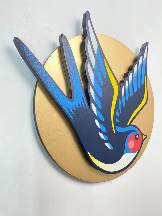 Angled photo of a handcrafted blue and yellow swallow wall art on a gold circle, by WallShapes, UK handmade decor.