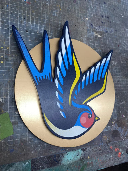 Handcrafted spray-painted wall art of a colorful swallow bird on a gold disk background.
